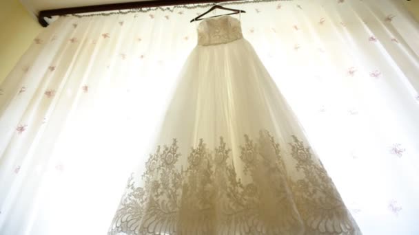 Fechar-se de um vestido de casamento na moda em um cabide, sapatos brancos no chão e um buquê com rosas rosa no quarto da noiva . — Vídeo de Stock