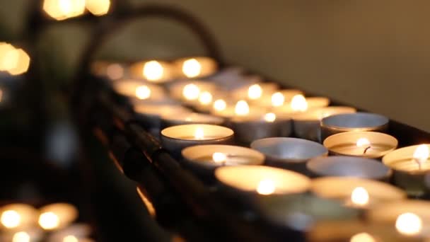 Beaucoup de bougies allumées sur une rangée dans une église . — Video