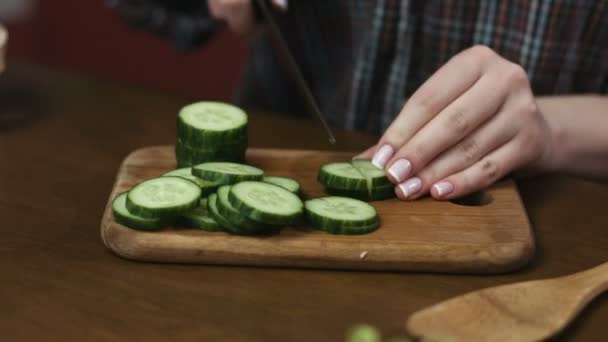 Vrouw met mooie nagels knippen komkommers ter voorbereiding van een salade op een snijplank. — Stockvideo
