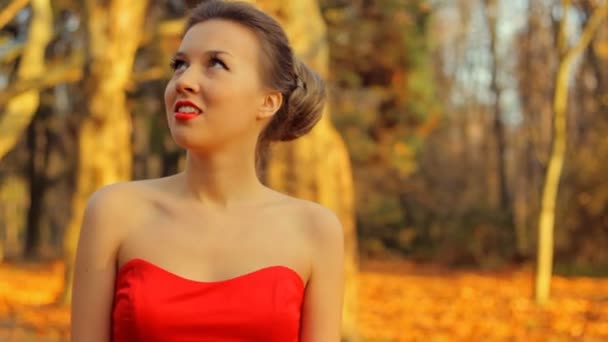 Hermosa mujer vistiendo vestido rojo y con maquillaje profesional caminar por el parque . — Vídeos de Stock