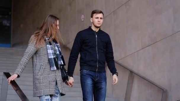 Young smiling woman and her serious handsome boyfriend moving down the stairs. — Stock Video