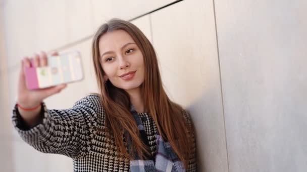 Giovane donna attraente indossa cappotto casual in bianco e nero sta prendendo selfie dal suo telefono cellulare per strada . — Video Stock