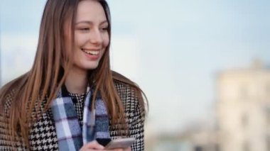 Onun smartphone ve gülümseme kullanarak çekici genç kadın sokakta.