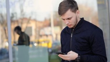 Yakışıklı ciddi adam sokakta akıllı telefonda mesajlaşma .