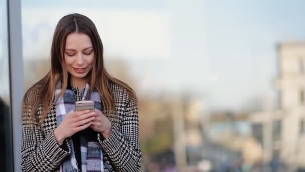 Mujer joven atractiva usando su teléfono inteligente y sonrisa en la calle . — Vídeo de stock