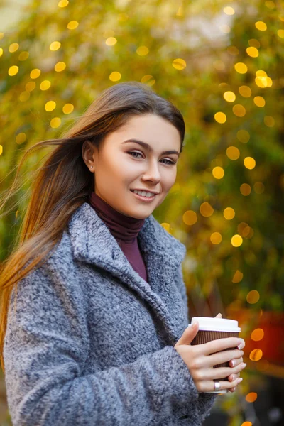 Vakker, smilende kvinne med en kopp kaffe i hendene i byen. – stockfoto