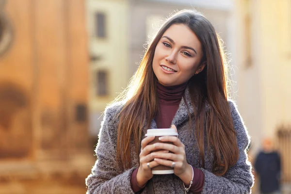 Hermosa mujer sonriente sosteniendo una taza de café en sus manos en la ciudad — Foto de Stock
