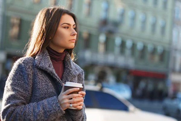 Hermosa mujer sonriente sosteniendo una taza de café en sus manos en la ciudad — Foto de Stock