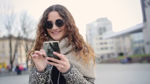 Imádnivaló fiatal mosolygó hölgy beszélget az utcán barátai fejhallgató. — Stock videók