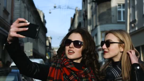 Dos adorables jóvenes amigos en gafas de sol tomando selfies en la calle . — Vídeo de stock