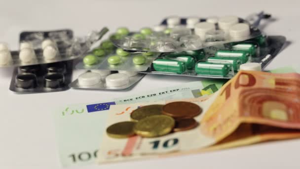 Medicine pills or capsules with money and syringe on white background. Pharmacy business, drug cost. Cash currency, expensive bill. Finance concept of pharmaceutical medication. Euro coins. — Stock Video
