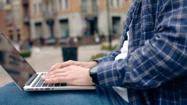 genç adam şehirde bankta otururken dizüstü bilgisayar üzerinde çalışan