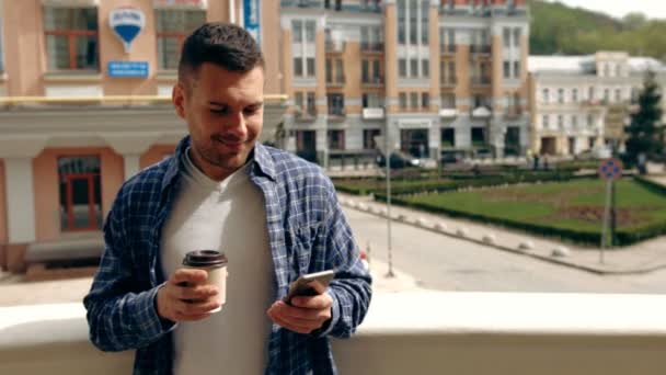 Joven disfrutando de un descanso para tomar café mientras usa su teléfono inteligente al aire libre . — Vídeos de Stock