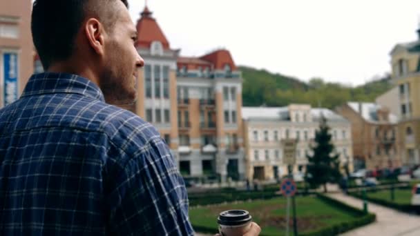 Style ville. Beau jeune homme en tenue décontractée intelligente tenant tasse de café et regardant loin tout en se tenant debout dans la rue — Video