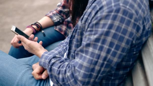 Молода пара сидить на лавці в місті і дивиться на смартфон — стокове відео