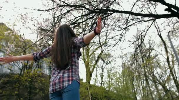 Glad leende brunett kvinna i rutig skjorta svarvning med armarna utsträckta utomhus — Stockvideo