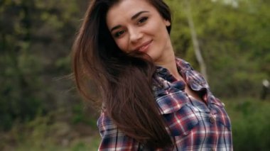 Damalı gömlek li ve açık havada poz veren çekici gülümseyen esmer kadın