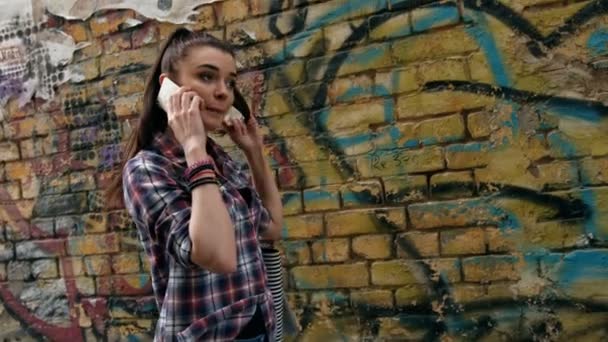 Ung kvinna med tal på mobiltelefon och röra vid hennes bruna hår när hon går på stadens gata — Stockvideo