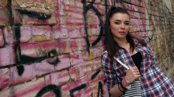 Porträt einer lächelnden schönen Modefrau im karierten Hemd und mit Pferdeschwanz gegen Graffiti-Wand — Stockvideo