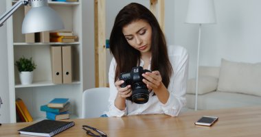 Ofisinde bir dijital fotoğraf makinesi bakarak beyaz gömlek gülümseyen güzel esmer fotoğraf editörü