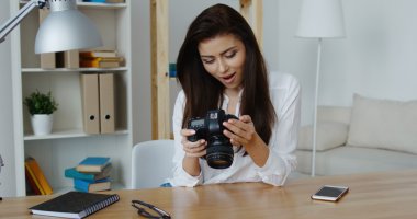 Ofisinde bir dijital fotoğraf makinesi bakarak beyaz gömlek gülümseyen güzel esmer fotoğraf editörü