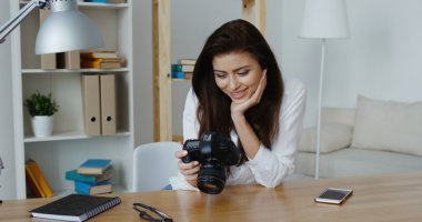 Ofisinde bir dijital fotoğraf makinesi bakarak beyaz gömlek gülümseyen güzel esmer fotoğraf editörü