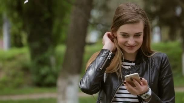 Menina incrivelmente bonita tocando seu cabelo ao usar seu telefone na rua  . — Vídeo de Stock
