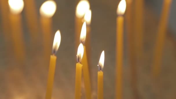 Gele kaarsen branden helder op de intreepupil achtergrond van een kerk. — Stockvideo