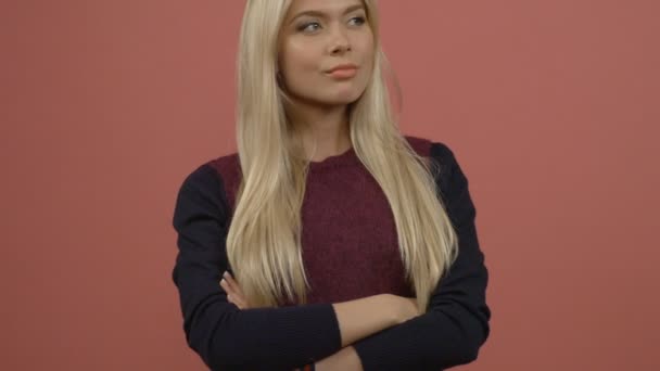 Retrato de media longitud de la hermosa rubia sonriente con suéter de marron de pie con los brazos cruzados mirándonos. Aislado sobre fondo rosa — Vídeos de Stock