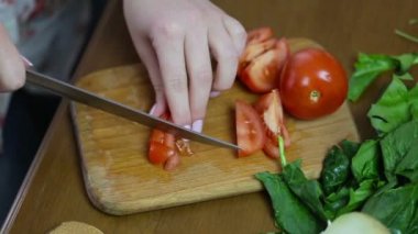 Bir kadın görüntüleri izleme eller Fransız çivi ile bir salata çatalı dilimlere domates kesme, yeşillik ve sebze yalan bir masada