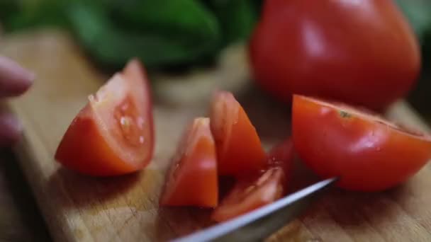 Imagens de rastreamento de uma mão feminina com unhas francesas estão cortando um tomate em fatias para fazer uma salada, verdura e legumes jazem em uma mesa. — Vídeo de Stock