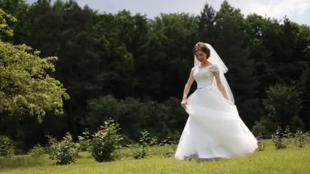 Hermosa morena bailando y dando vueltas con vestido de novia en el parque — Vídeo de stock