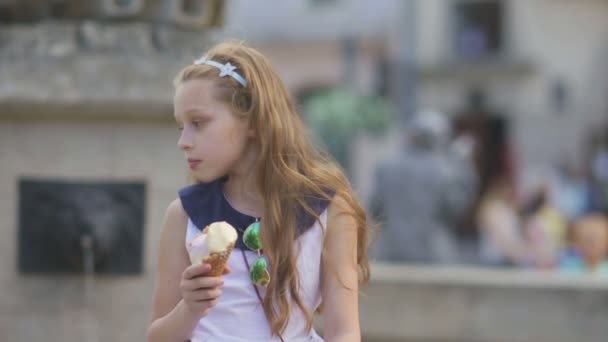 Маленькая девочка ест мороженое в жаркий, жаркий летний день на детской площадке в парке, дети — стоковое видео