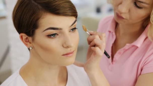 Maquiagem artista aplicando pó com maquiagem escova para bela mulher morena com corte de cabelo curto, close-up — Vídeo de Stock