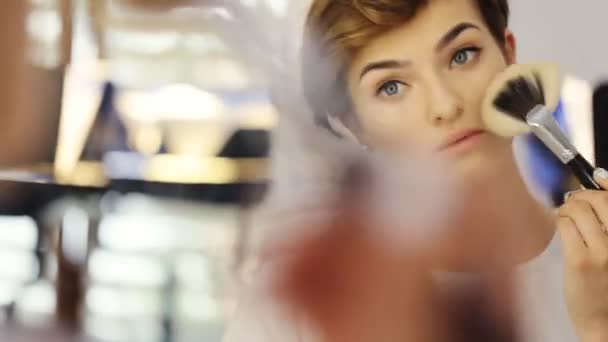 Mujer de belleza aplicando maquillaje. Hermosa chica mirando en el espejo y la aplicación de cosméticos en los pómulos con un cepillo grande — Vídeo de stock