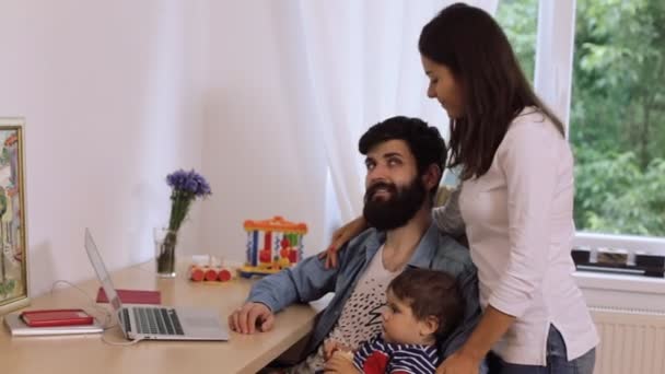 Feliz jovem casal com filho usando laptop na mesa, jovem mulher beijando barbudo homem — Vídeo de Stock