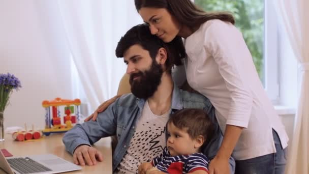 Happy young couple with son using laptop at desk, young woman kissing bearded man — Stock Video