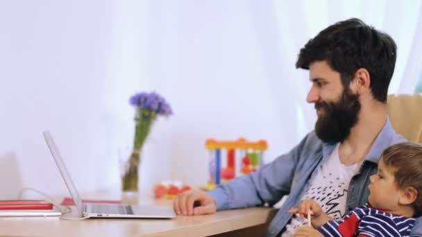 Family time. Young smiling bearded father and his cute son using computer together at home — Stock Video