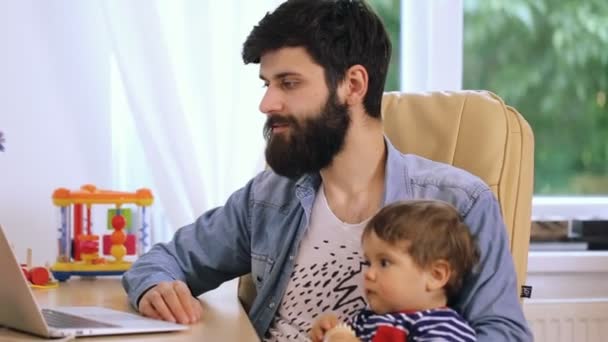 Tempo in famiglia. Giovane padre barbuto sorridente e il suo figlio carino utilizzando il computer insieme a casa — Video Stock