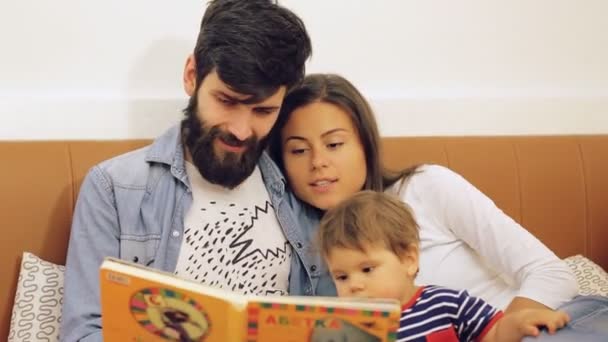 Счастливая семья с симпатичным мальчиком, читающим книгу перед сном — стоковое видео