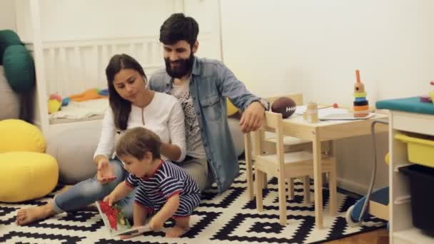 Jonge ouders pappa en mamma lezen kinderen boek aan zoontje over de vloer thuis — Stockvideo