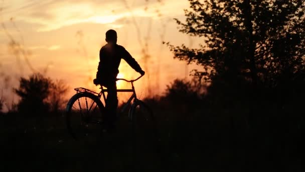 Мальчик едет на велосипеде в деревню, пока солнце садится.  . — стоковое видео