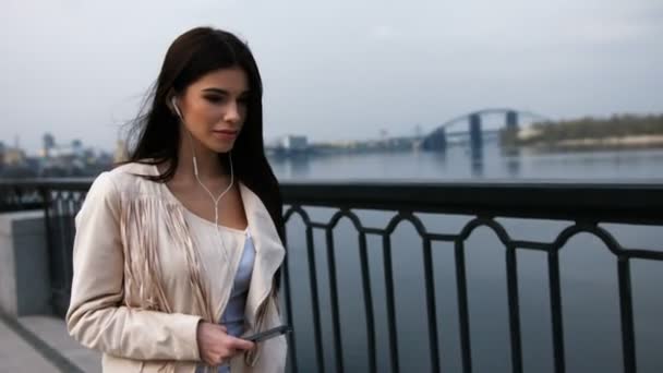 Joven mujer feliz relajándose al aire libre caminando en un puente moderno mientras escucha música . — Vídeos de Stock