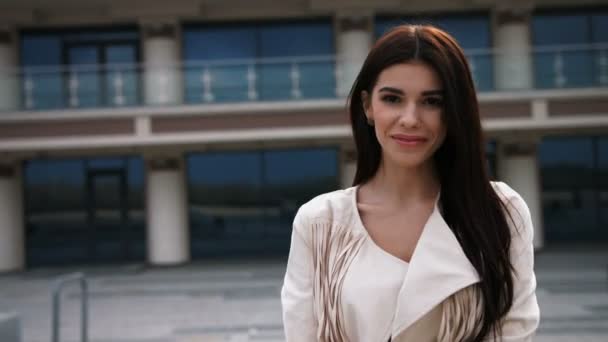 Retrato de moda al aire libre de la bonita morena elegante riendo mujer en chaqueta blanca y maquillaje natural. Fondo urbano europeo. Mirada de calle . — Vídeo de stock