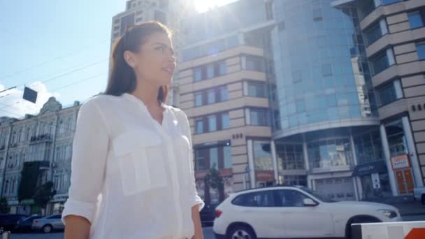 Vista lateral de hermosa mujer en camisa blanca y con pelo largo oscuro caminando por las calles urbanas de la ciudad — Vídeos de Stock