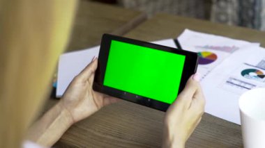Kadın elleri tablet-pc ile ofiste çalışan, ahşap masa, yakın çekim. Ekranın yeşil bir ekranı var