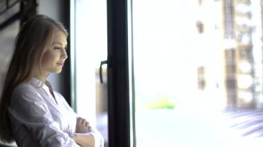 Kolları çapraz ve pencere yakınında düşünme ile ayakta beyaz gömlek li kendine güvenen kadının yakın çekim portre.