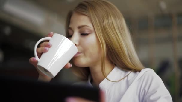 Ganska blondin med kaffe medan du använder tabletten på kaféet, närbild — Stockvideo