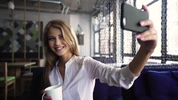 Hermosa mujer rubia en camisa blanca tomando selfie taza de celebración en la barra de café . — Vídeos de Stock