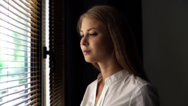 Obrázek zblízka s krásnou blonďatou mladou ženou v bílé blůze s šťastným úsměvem při pohledu na kameru na sluneční osvětlovací pozadí okna — Stock video